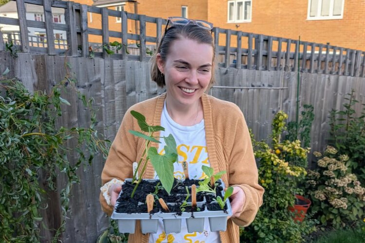 Nathalie smiling holding a tray of plants in a garden