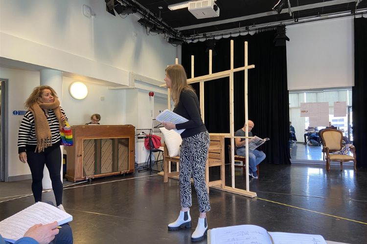 Rehearsal behind the scenes - two females are standing facing each other approx 6 feet apart. They appear to be talking and one is holding a script.