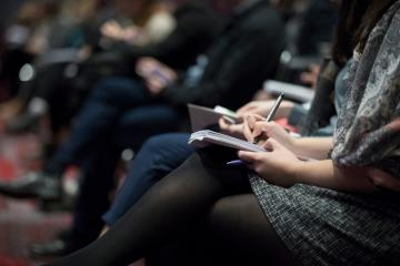 People writing in notebooks at a conference